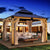 Elegant wooden gazebo with curtains, cozy seating, and soft lighting at dusk.